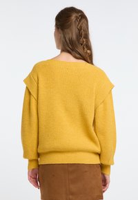 Hosszú ujjú, oversized pulóver élénk sárga színben, bordázott textúrával, ejtett vállakkal és széles nyakkivágással. A corduroy szoknya látható alatta.