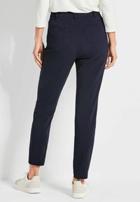 Marineblauwe broek met een slim fit, voorzien van twee achterzakken en een tailleband, gecombineerd met witte sneakers op een neutrale achtergrond.