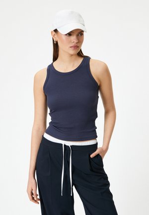 Camiseta de tirantes de rayas en color navy con escote redondo, combinada con pantalones holgados oscuros que tienen un cordón blanco y pliegues horizontales.