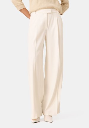 Pantalons larges plissés en tissu crème clair. Texture lisse, taille cintrée. Assortis à des talons sculptés dans une teinte coordonnée.