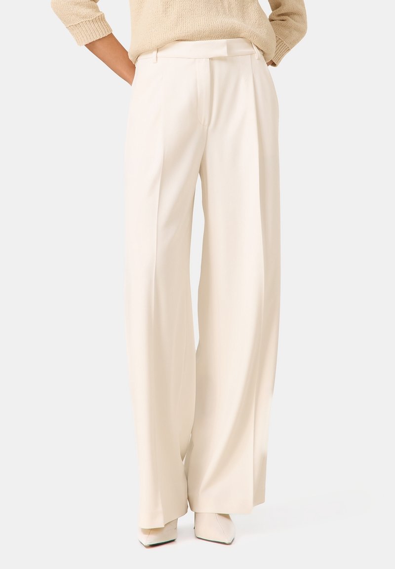 Pantalons larges plissés en tissu crème clair. Texture lisse, taille cintrée. Assortis à des talons sculptés dans une teinte coordonnée.