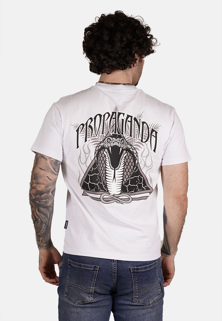 T-shirt bianco in cotone con una grande grafica di un serpente nero sul retro, con dettagliati squame e la parola "PROPAGANDA" in carattere grassetto sopra.