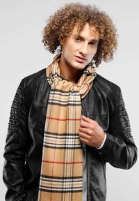 Tan plaid scarf with black and red accents, made of soft fabric, layered over a black leather jacket with ribbed shoulder detailing.