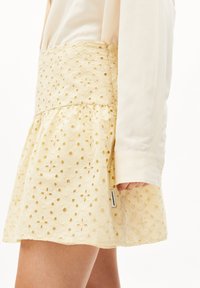 Jupe mini jaune brodée avec un motif floral texturé, une taille ajustée et un ourlet évasé. Comprend une étiquette de marque sur le côté.