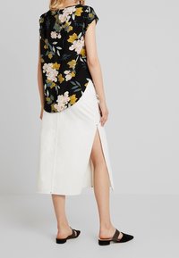 Černá květinová blůza s krátkými rukávy, doplněná bílou denimovou sukní s postranním rozparkem. Outfit dokreslují černé skluzné sandály.