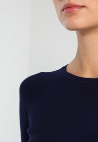 Pull côtelé bleu marine avec un col rond et des manches raglan, présentant une texture douce et une silhouette ajustée.