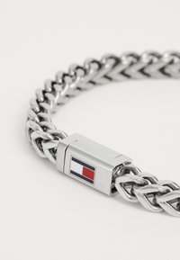 Sølvmetall lenkearmbånd med flettet design og rektangulært spenne med blå, hvite og røde detaljer.