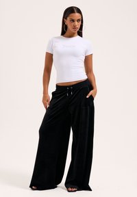 Weißes, kurzärmliges, figurbetontes Oberteil mit "Juicy"-Schriftlogo, kombiniert mit schwarzen, weit geschnittenen Hosen aus weichem Stoff mit Kordelzugbund und seitlichen Taschen.