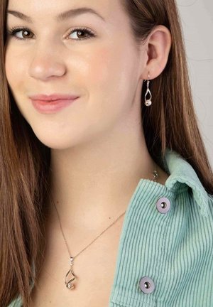 Zilveren druppeloorbellen met een parel detail en een bijpassende hangerketting. Model draagt een mintgroene top met koord en drukknopen.
