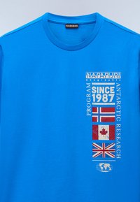 Modrá bavlněná trička s textem a grafikou, včetně vlajek Norska, Kanady a Spojeného království. Design s kulatým výstřihem; hladká textura.