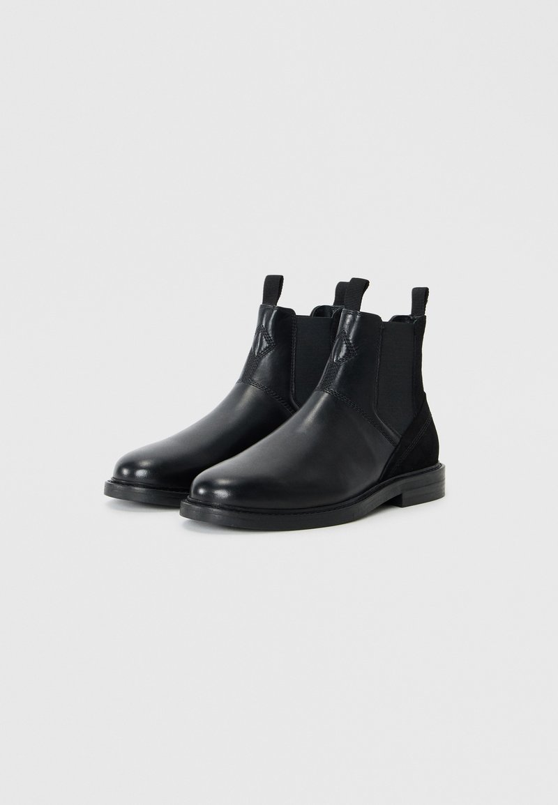 Schwarze Lederstiefeletten mit elastischen seitlichen Einsätzen, runder Zehenform und strukturierten schwarzen Wildlederakzenten. Robuste schwarze Gummisohle.