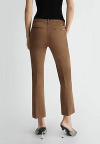 Pantaloni marroni aderenti con una texture liscia, dotati di due tasche posteriori e chiusura con zip. Abbinati a mule nere con tacco.