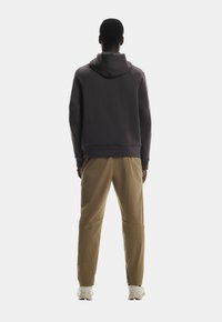 Tumehall hallitus, millel on suur kapuuts, koos beežide pükstega, millel on kitsenev lõige. Hallitusel on ribaga mansetid ja ääred.