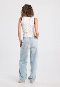White tank top with dark trim and light blue wide-leg jeans. The jeans feature rear pockets and a label on the waistband. Plain background.