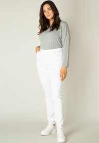 Grijze langemouwen top met een ronde hals, gecombineerd met hoge witte jeans en witte sneakers. Eenvoudig ontwerp, gladde textuur.