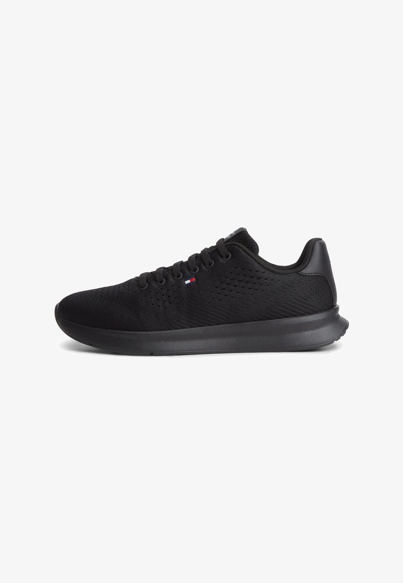 Baskets de sport légères noires avec tige en mesh, semelle noire, design à lacets et petit logo rouge, blanc et bleu sur le côté.