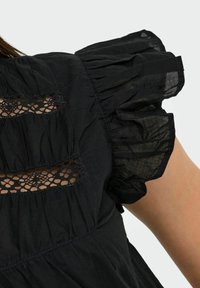 Black blouse featuring puffed sleeves, textured lace inserts, and a flowing silhouette. Made from lightweight fabric with a wrinkled appearance.