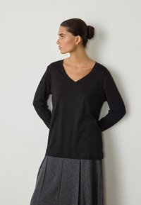 Czarna bluzka z długim rękawem i dekoltem w serek, wykonana z miękkiej tkaniny, o luźnym kroju i gładkiej fakturze, zestawiona z teksturowaną, szarą plisowaną spódnicą.