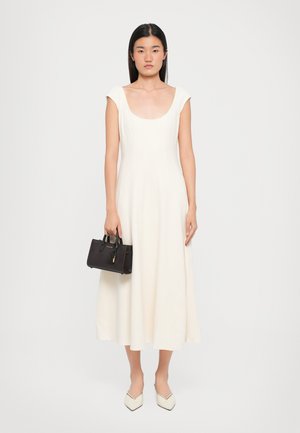 A fitted, cream-colored dress with cap sleeves and a scoop neck, paired with a small black handbag and pointed white flats.
