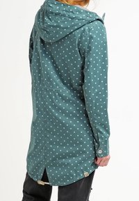 Wodoodporny zielony płaszcz w jasnoniebieskie kropki, z kapturem na sznurku i zatrzaskami na mankietach. Posiada wentylowany tył i regulowany dół.