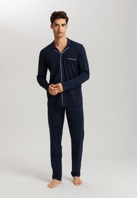 Navy blue miesten pyjamapuku pehmeästä kankaasta, jossa on pitkät hihat, napillinen paita taskulla ja kontrastivalkoiset yksityiskohdat.