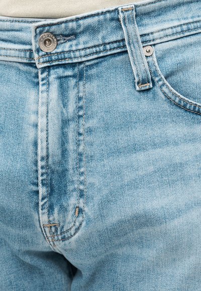 Τζιν σε ανοιχτό γαλάζιο χρώμα με κλείσιμο με κουμπί, ελαφρύ ξεθώριασμα και δομημένες ραφές. Διαθέτει μία θηλιά στην μέση και εμπρός τσέπες.