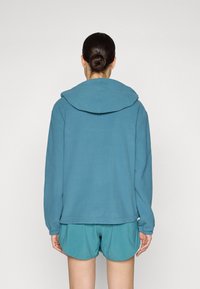 Blue hoodie with a large hood, made of soft fabric. Worn with matching short shorts. Simple, relaxed fit, with long sleeves and a straight hem.