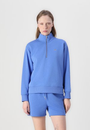 Light blue zip-up sweatshirt with high collar and ribbed cuffs, paired with matching shorts featuring a drawstring waistband. Simple design.