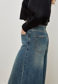 Wijde denim jeans met een vervaagde blauwe wasm, hoge taille en klassieke achterzakken, gecombineerd met een zwart geribbeld brei-sweater.