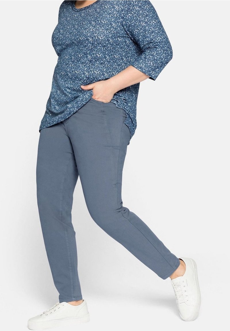 Haut bleu à motif floral avec manches trois-quarts, associé à un pantalon bleu clair et des chaussures blanches. Le pantalon présente une coupe droite.