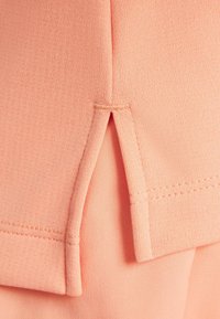 Materiał w kolorze brzoskwiniowym o żeberkowanej fakturze, z bocznym rozcięciem i starannymi przeszyciami. Prosty i elastyczny design zapewniający komfort.