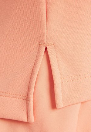 Pfirsichfarbenes Gewebe mit gerippter Struktur, versehen mit einem seitlichen Schlitz und sauberer Nahtführung. Einfaches und flexibles Design für Komfort.