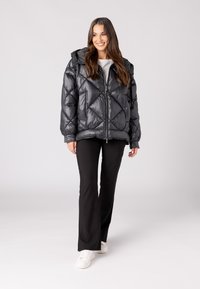Zwarte, gewatteerde puffer jas met capuchon, voorzien van een ritsluiting en een scherp diagonaal stikselpatroon. Draag deze over een zwarte broek en witte sneakers.