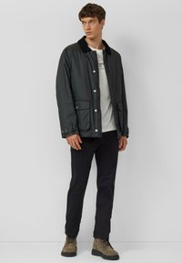 Czarna lekka kurtka z kołnierzem ze sztruksu, zatrzaskami i bocznymi kieszeniami, noszona na jasnym t-shircie i czarnych spodniach, w połączeniu z butami.