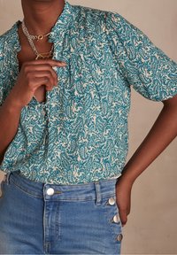 Blusa a maniche corte con un motivo paisley in tonalità teal e crema, con dettaglio arricciato all'escollatura e bottoni sul lato sinistro.