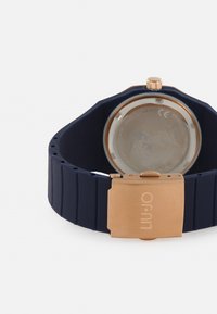 Orologio in silicone blu navy con cinturino testurizzato e chiusura in metallo color oro rosa; il fondello trasparente rivela il meccanismo del orologio.