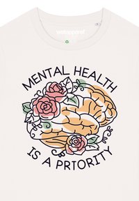 T-shirt couleur crème avec un graphique de cerveau, décoré de roses roses et vertes, et le texte "LA SANTÉ MENTALE EST UNE PRIORITÉ" en noir.