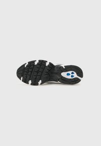 Semelle de chaussure de sport en noir et blanc avec des rainures saillantes et une texture antidérapante. Elle présente des accents bleus dans la zone du talon et des formes arrondies.