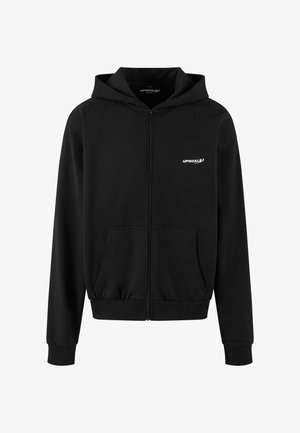 Musta tõmblukuga kapuutsiga jakk, mis on valmistatud pehmest kangast. Sellel on ees tasku, soonikkoes mansetid ja vasakul rindkerel valge "UPSCALE" logo.