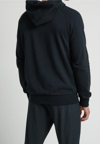 Hoodie noir avec une capuche spacieuse, des poignets et un ourlet côtelés. Fabriqué en tissu doux avec une texture lisse, offrant une coupe décontractée.