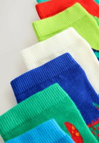 Pila de calcetines acanalados de colores con puños visibles en tonos rojo, verde, blanco, azul y turquesa sobre un fondo claro.