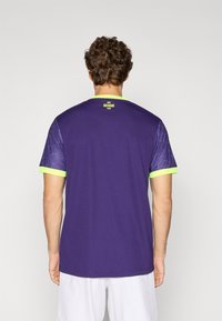 T-shirt de sport violet à manches courtes. Présente un design texturé et à motifs sur les manches, avec un col et des accents verts vif.