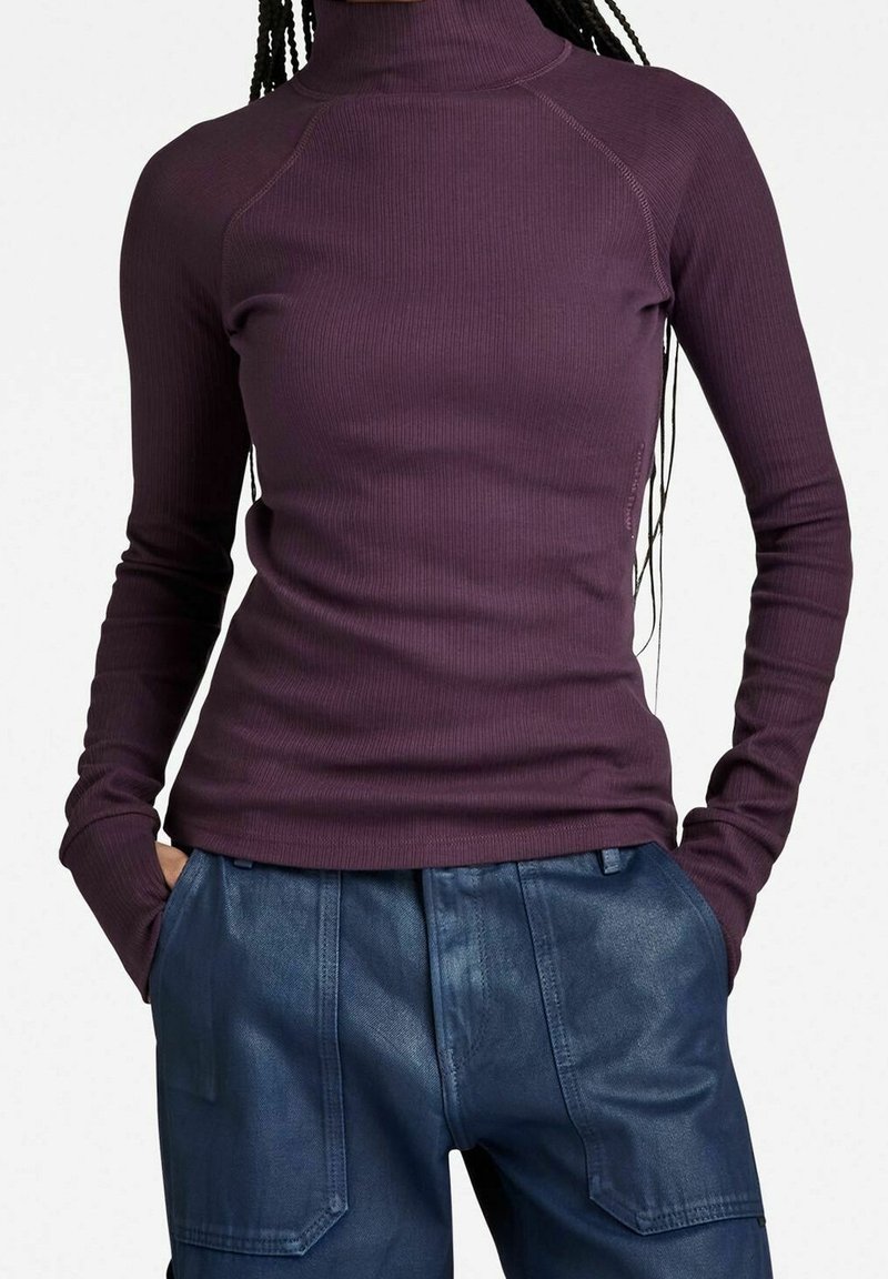 Lila ribbad polotröja med långa ärmar och raglan sömmar, i kombination med blå texturerade byxor med fickor.