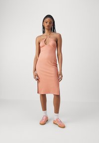 Robe midi à bretelles côtelées en pêche douce avec un décolleté en trou de serrure et des fentes sur les côtés, portée avec des baskets roses et des chaussettes blanches.