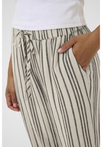 Striped pants in light beige with dark gray vertical stripes. Features an elastic waist, drawstring, and side pockets. Textured fabric.