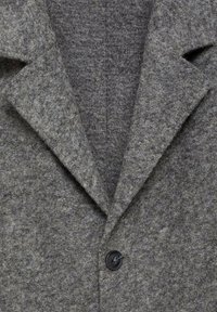 Cappotto grigio in feltro con ampi rever, chiusura con un singolo bottone nero e un tessuto texture. Il design presenta linee pulite e una vestibilità su misura.