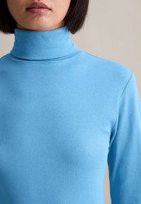 Helles blaues, geripptes Rollkragenoberteil, enganliegendes Design mit langen Ärmeln, glatte Textur, minimale Details, geeignet zum Schichten.