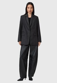Blazer grigio scuro con vestibilità su misura, rever a punta, chiusura frontale con bottone e due tasche laterali, abbinato a pantaloni in pelle a gamba larga.