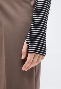 Hele nahaga käsi must-valge triibulise varrukast, toetudes pruuni kangaseina vastu.