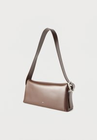 Κομψή καφέ δερμάτινη τσάντα ώμου με καμπύλο καπάκι, ασημένια αγκράφα σε ρυθμιζόμενο λουρί και διακριτικό λογότυπο στο κέντρο μπροστά.